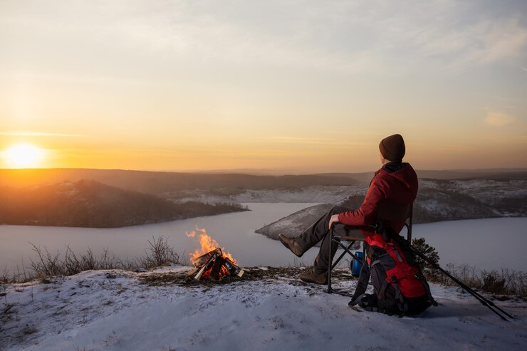 Cold Comfort: A Camping Guide to Snowy Survival 2025 5 man-hiker-sitting-top-mounting-near-campfire-enjoying-yellow-sunset-winter-nature-travel-lifestyle-freedom-concept